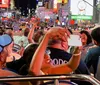 Tourists on an open-top bus at night are taking photos of the vibrant street scenes and bright neon lights in Times Square New York