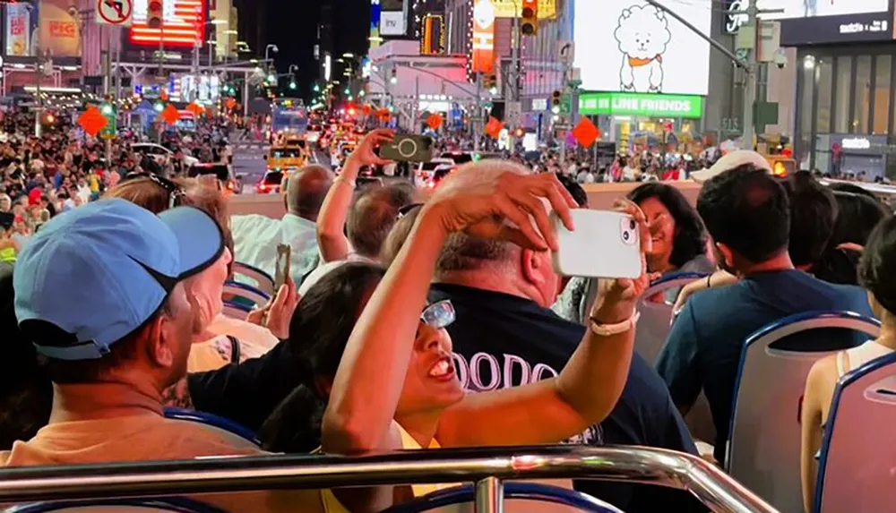 Tourists on an open-top bus at night are taking photos of the vibrant street scenes and bright neon lights in Times Square New York