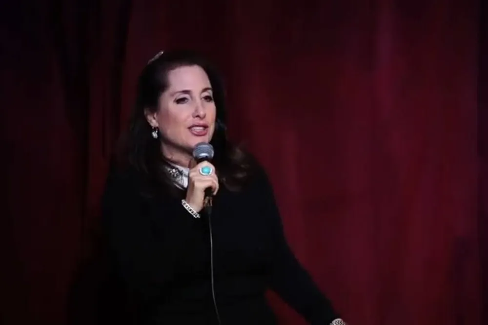 A woman is speaking into a microphone against a backdrop of red curtains likely during a presentation or performance