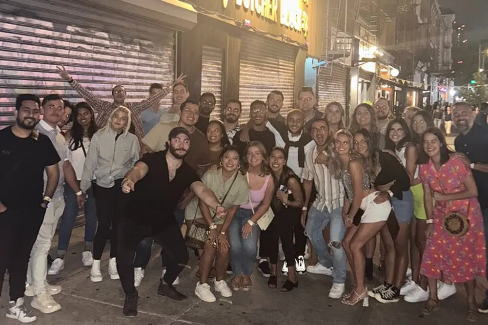 A large group of smiling people posing for a photo on a lively urban street at night