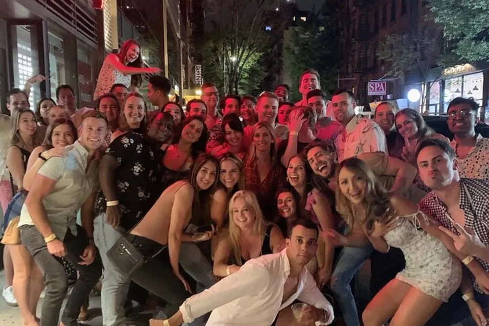 A large diverse group of people are gathered together posing playfully for a casual group photo at night