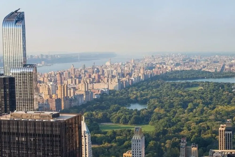 An aerial view of Central Park enveloped by the urban landscape of New York City with a skyscraper in the foreground