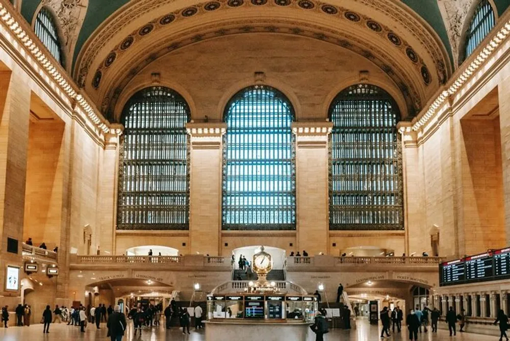 The image shows the spacious interior of a grand train station with high ceilings large windows and a bustling concourse area with passengers and an information booth likely captured during a moment of relative calm