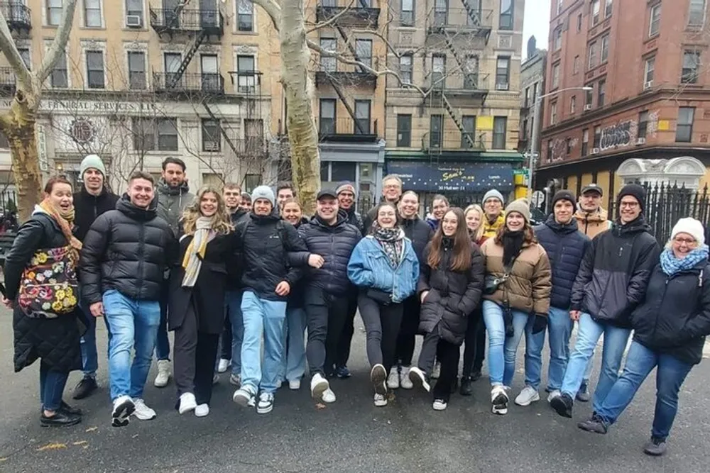 A group of people are posing for a photo on a city street smiling and dressed in warm clothing