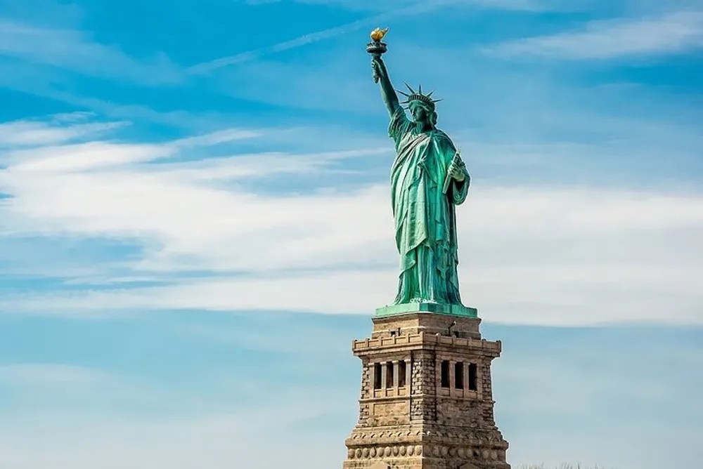 The Statue of Liberty stands tall against a blue sky with wispy clouds