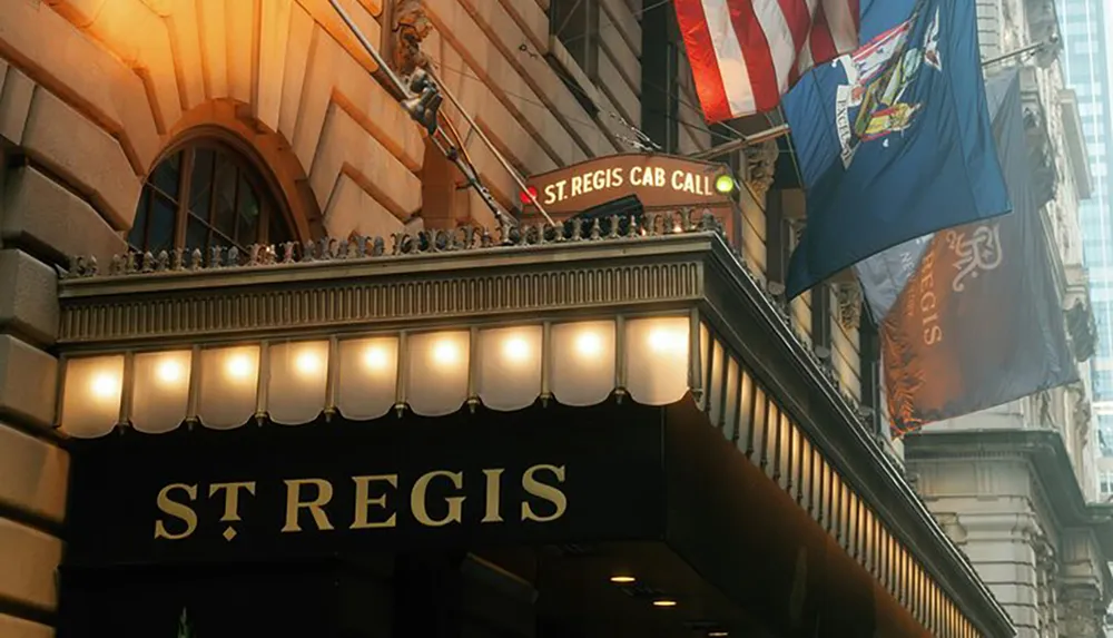 The image shows the illuminated marquee sign of the St Regis hotel with flags flying above it