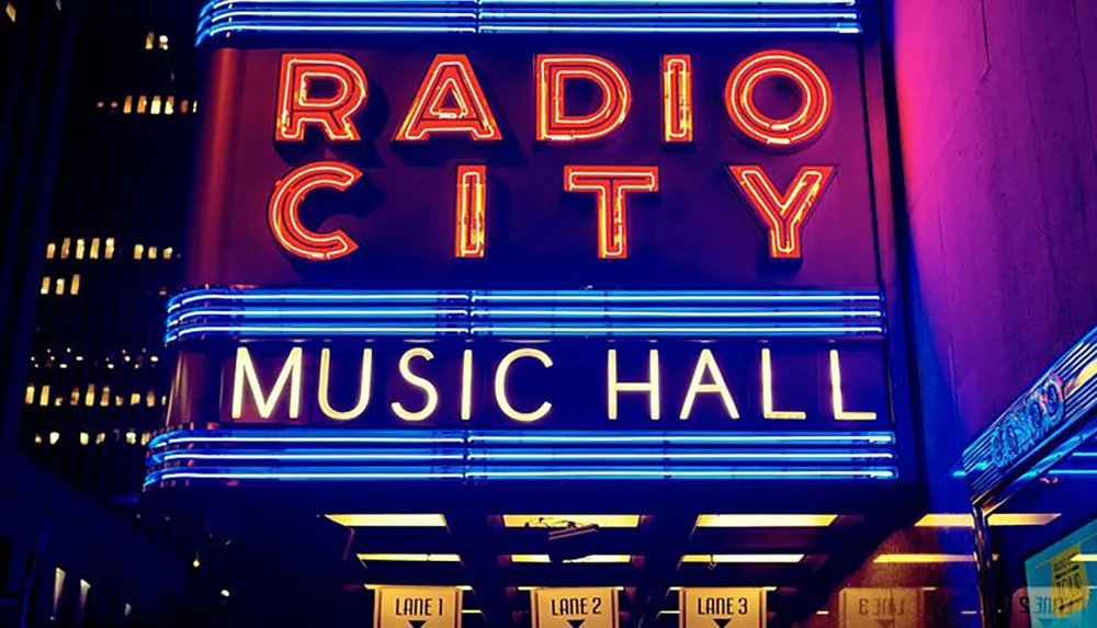 The image displays the vibrant neon marquee of Radio City Music Hall illuminated at night