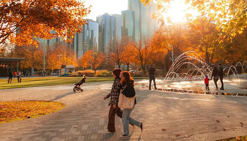 People enjoy a sunny autumn day in a park with a fountain and colorful trees with a backdrop of skyscrapers