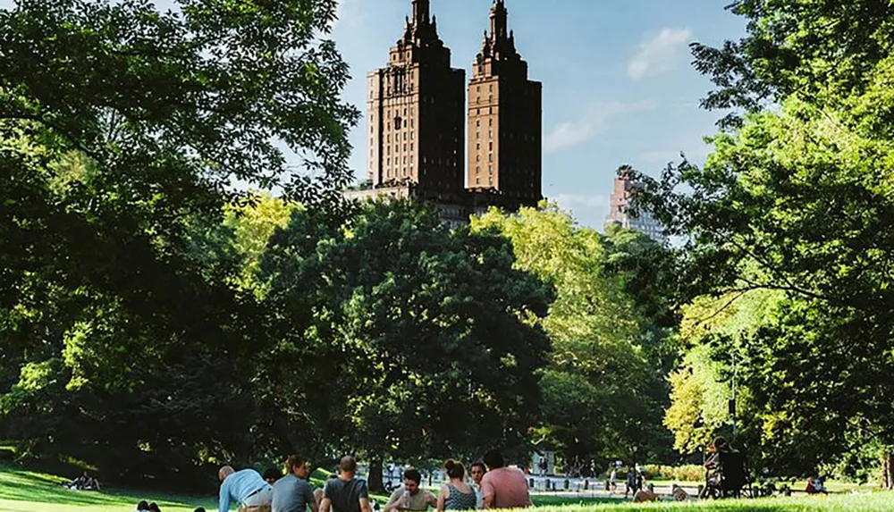 People are enjoying a sunny day in a lush park with tall buildings looming in the background