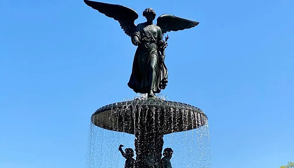 The image features an angel statue atop a fountain with water cascading down into the basin below against a clear blue sky