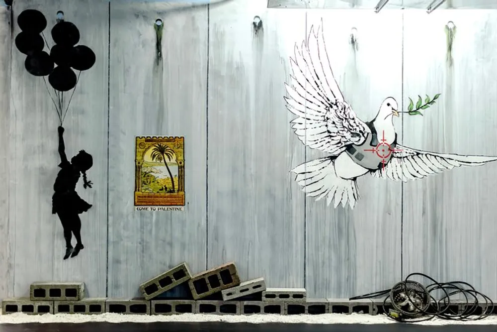 This image features a mural depicting a silhouette of a child holding balloons next to a vintage Come to Palestine poster with a dove wearing a bulletproof vest and toppled chairs and unraveled film reels against a weathered wall backdrop