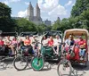 A group of smiling people enjoys a sunny day on a pedicab tour with a view of a tall historic building in the background