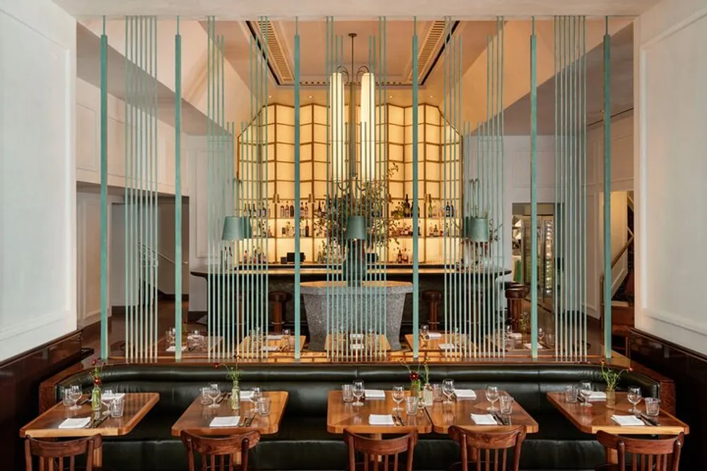 The image depicts an elegantly designed restaurant interior with set tables green upholstered benches wooden chairs and an ornate bar area framed by decorative vertical green elements