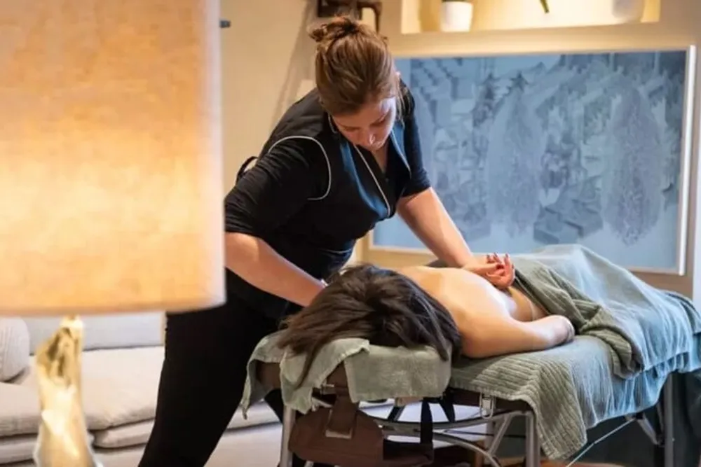 A massage therapist is performing a back massage on a client who is lying face down on a massage table