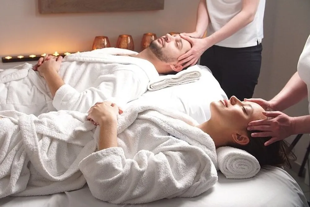 A man and a woman are lying down receiving relaxing head massages in a serene spa setting