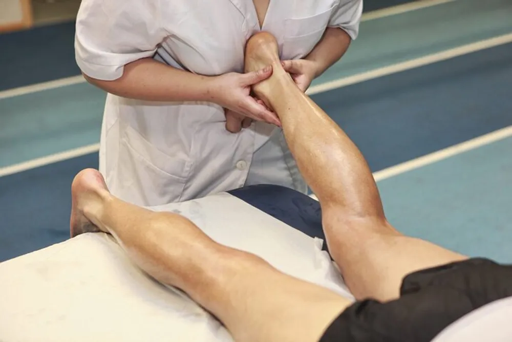 A healthcare professional appears to be examining or treating a persons leg in a clinical or sports therapy setting