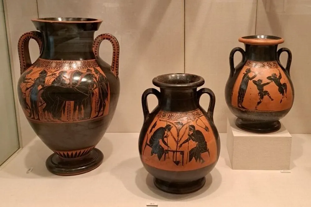 The image shows three ancient Greek vases with black-figure pottery designs displayed in a museum setting