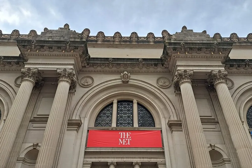 The image shows the neoclassical facade of The Metropolitan Museum of Art in New York highlighted by its iconic THE MET banner