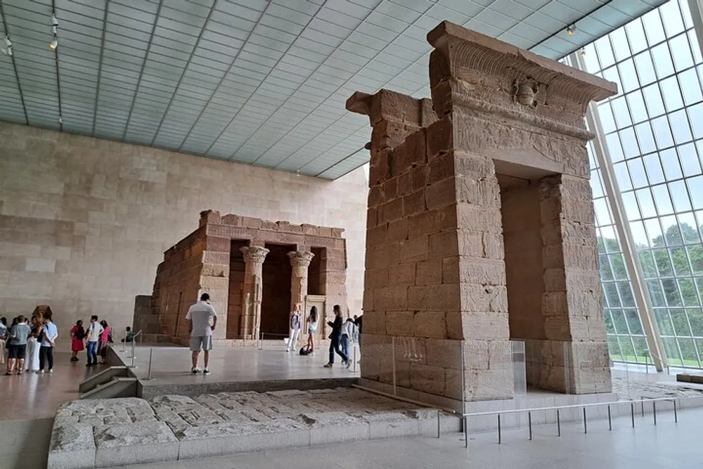 Visitors are exploring the ancient Temple of Dendur displayed within a large light-flooded room of a museum