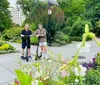 Two individuals and two electric scooters are standing on a rock with a pond and an arched bridge in the background