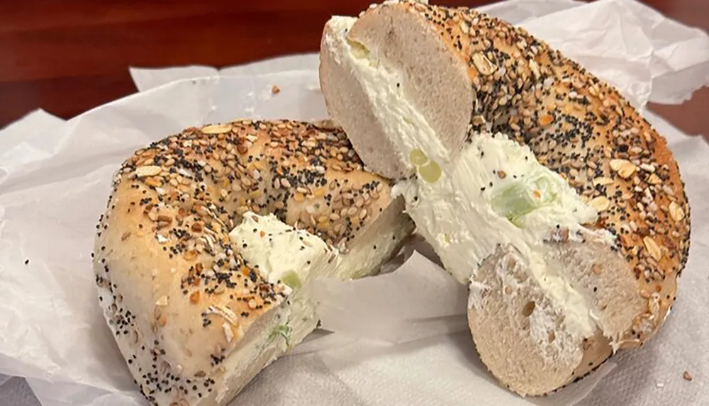 A sliced everything bagel spread with cream cheese is lying on white paper