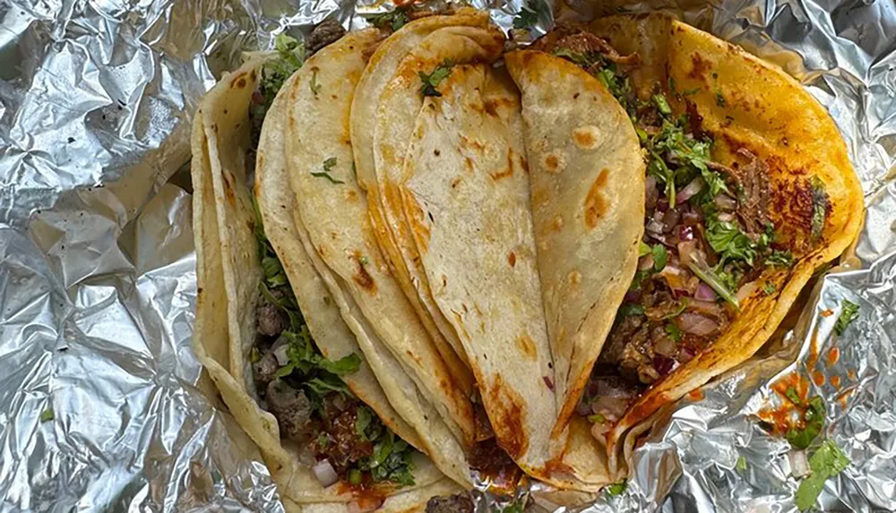 The image shows a row of tacos with visible fillings of meat onion and cilantro resting on foil