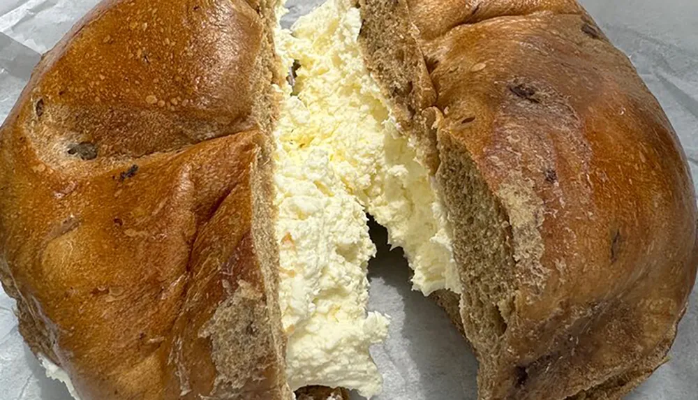 The image shows a bagel sliced horizontally with an excessive amount of cream cheese filling