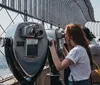 A person is looking through a coin-operated binoculars at a high vantage point with other visitors around