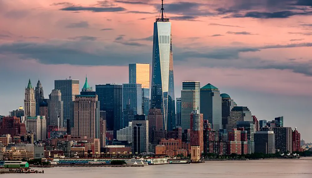 The image shows a skyline view of Lower Manhattan at dusk with the One World Trade Center standing prominently against a backdrop of colorful sky and clouds