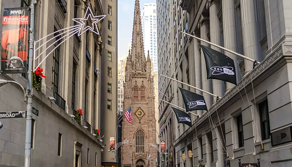 The image captures a narrow urban street flanked by tall buildings adorned with holiday decorations leading to a gothic-style church with flags and a star-shaped light display visible