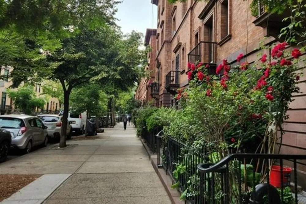 A tranquil city sidewalk lined with lush green trees red flowers and classic brick buildings