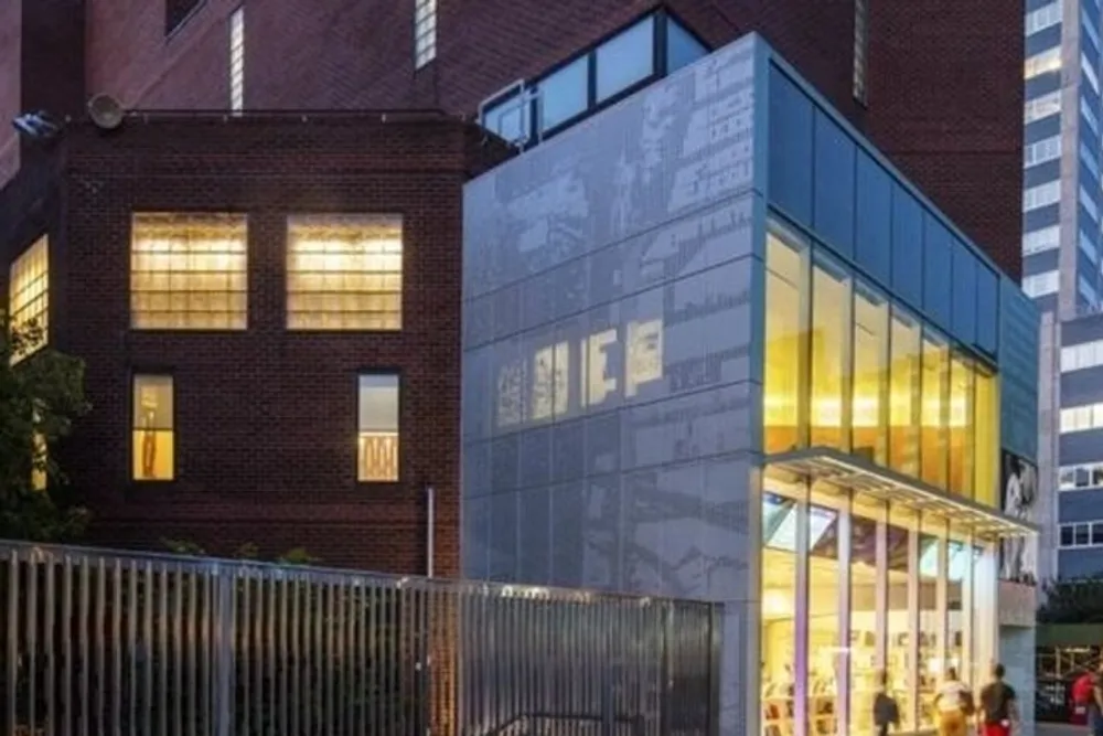 The image shows a modern glass extension juxtaposed with an older brick building illuminated in the evening