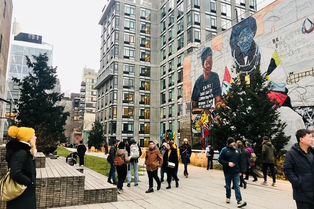 People stroll by a modern building with an artistic mural near a Christmas tree in an urban park setting