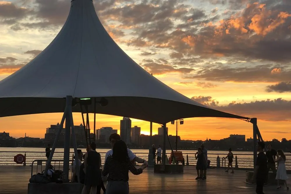 People are enjoying a vibrant sunset by the waterfront under a large canopy