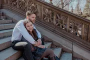 A couple is sharing an intimate moment of closeness while sitting on stone steps, giving the impression of happiness and affection.