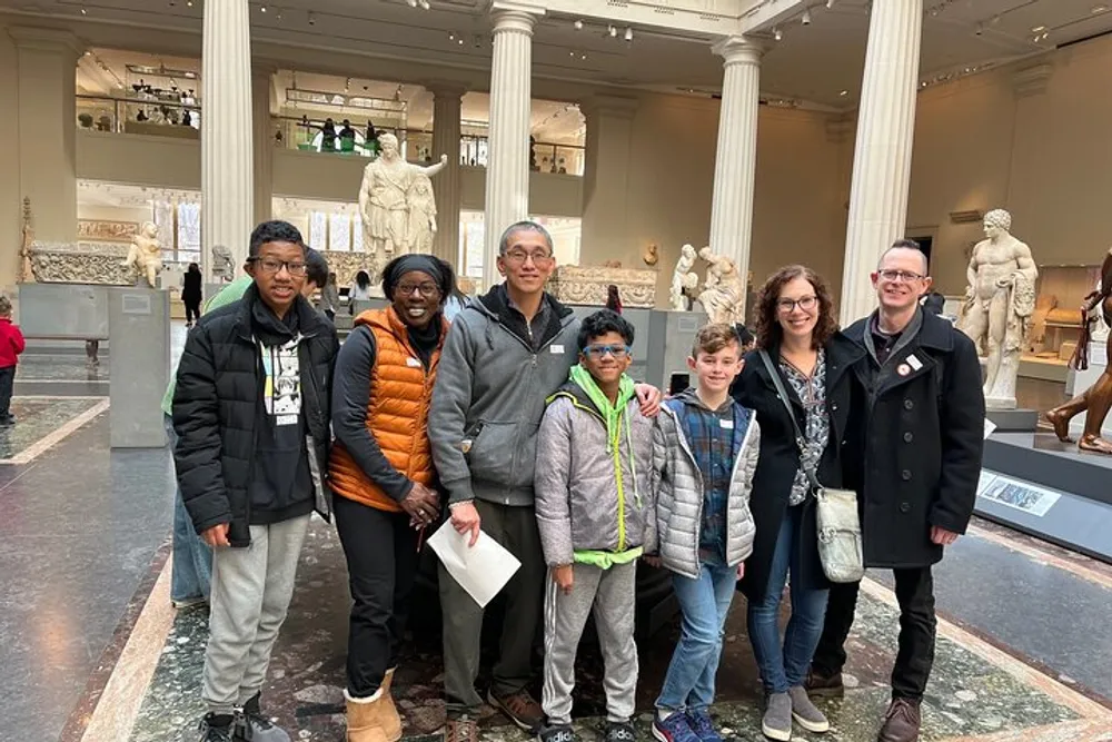 A group of seven people is posing for a photo in a museum gallery filled with classical statues