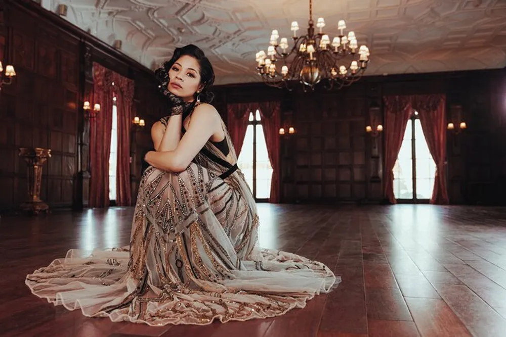 A person is posing in an elegant beaded dress in a grand room with a vintage aesthetic