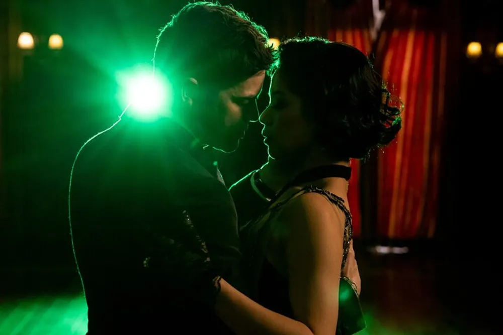 A man and woman are sharing an intimate dance moment on a dimly lit dance floor with a spotlight behind them