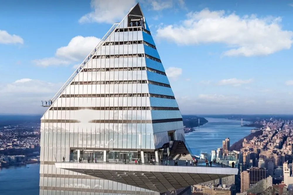 The image shows an architectural design of a modern pyramid-shaped skyscraper with a viewing platform set against a backdrop of an urban riverfront cityscape