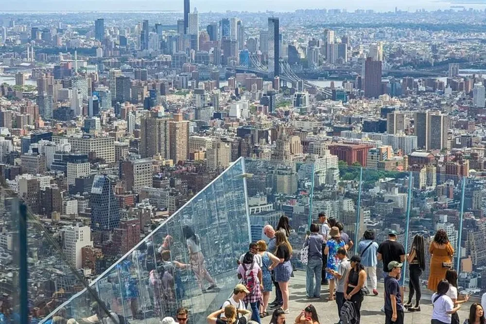 Visitors enjoy a panoramic view of a dense urban skyline from a high vantage point with transparent barriers