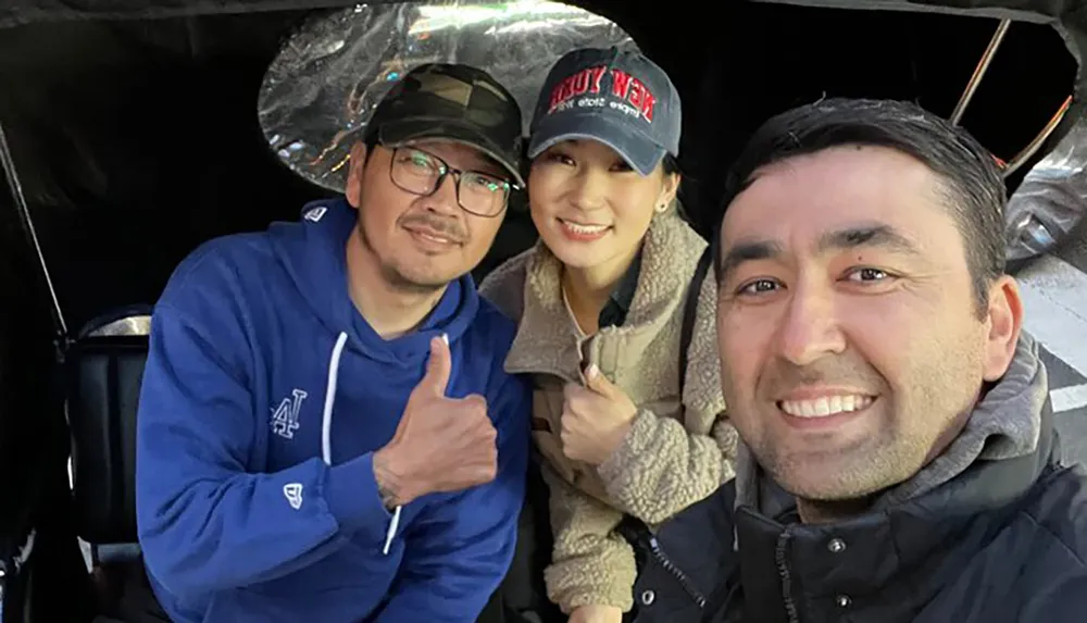 Three people are smiling for a selfie with two of them showing thumbs-up signs to the camera