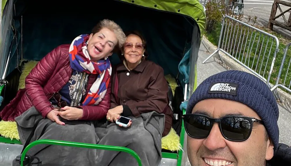 Three people are sharing a joyful moment in a rickshaw with two seated inside and one taking a selfie from the front