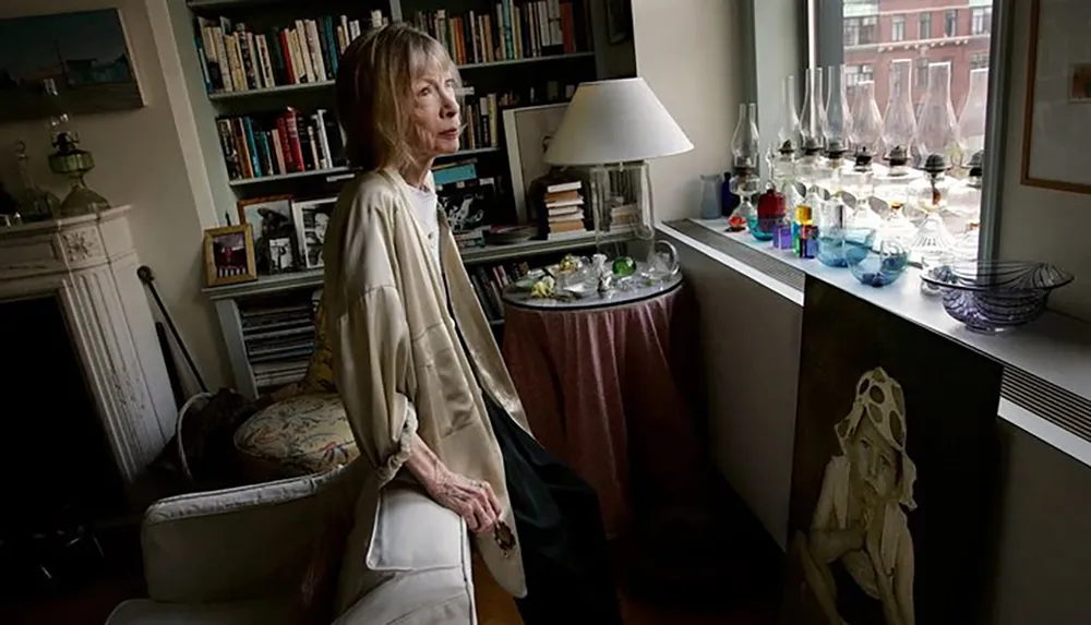 A woman stands contemplatively in a cozy book-filled room with an elaborate collection of glassware displayed on a windowsill