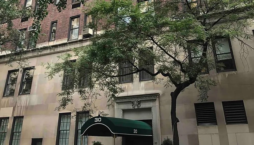 The image shows the front of an urban building with the number 30 prominently displayed above the entrance flanked by green trees and featuring several air conditioning units in the windows