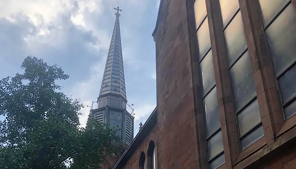 The image shows the side of a brick church with a tall steeple against a partly cloudy sky