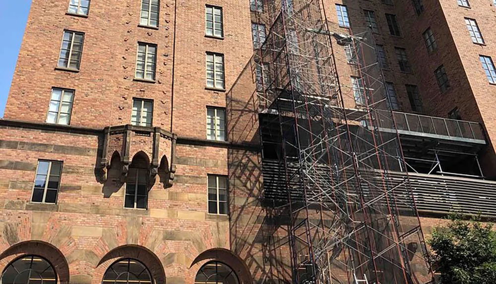 This image shows a tall brick building with scaffolding erected alongside it possibly for maintenance or construction purposes