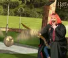 A person with pink hair is sitting on a broom wearing a Hogwarts robe and laughing as they seemingly play Quidditch in a Harry Potter-themed setting