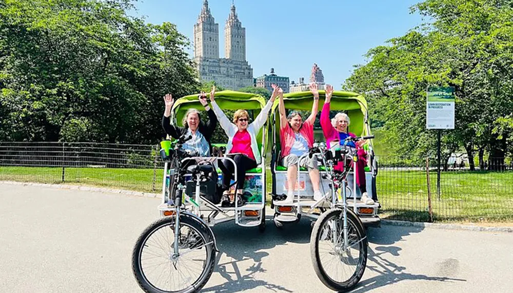 A group of people is cheerfully posing on a pedal-powered rickshaw-like vehicle in a park with tall buildings in the background