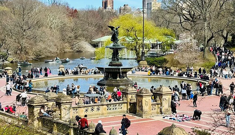 The image shows a bustling scene at a park with people enjoying the sunny weather by the edge of a pond some rowing boats and others lounging near a fountain