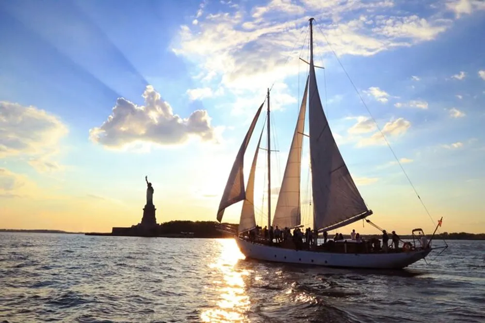 A sailboat is gliding across the water near the Statue of Liberty during a beautiful sunset